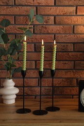 Photo of Candlesticks with burning candles on table near brick wall