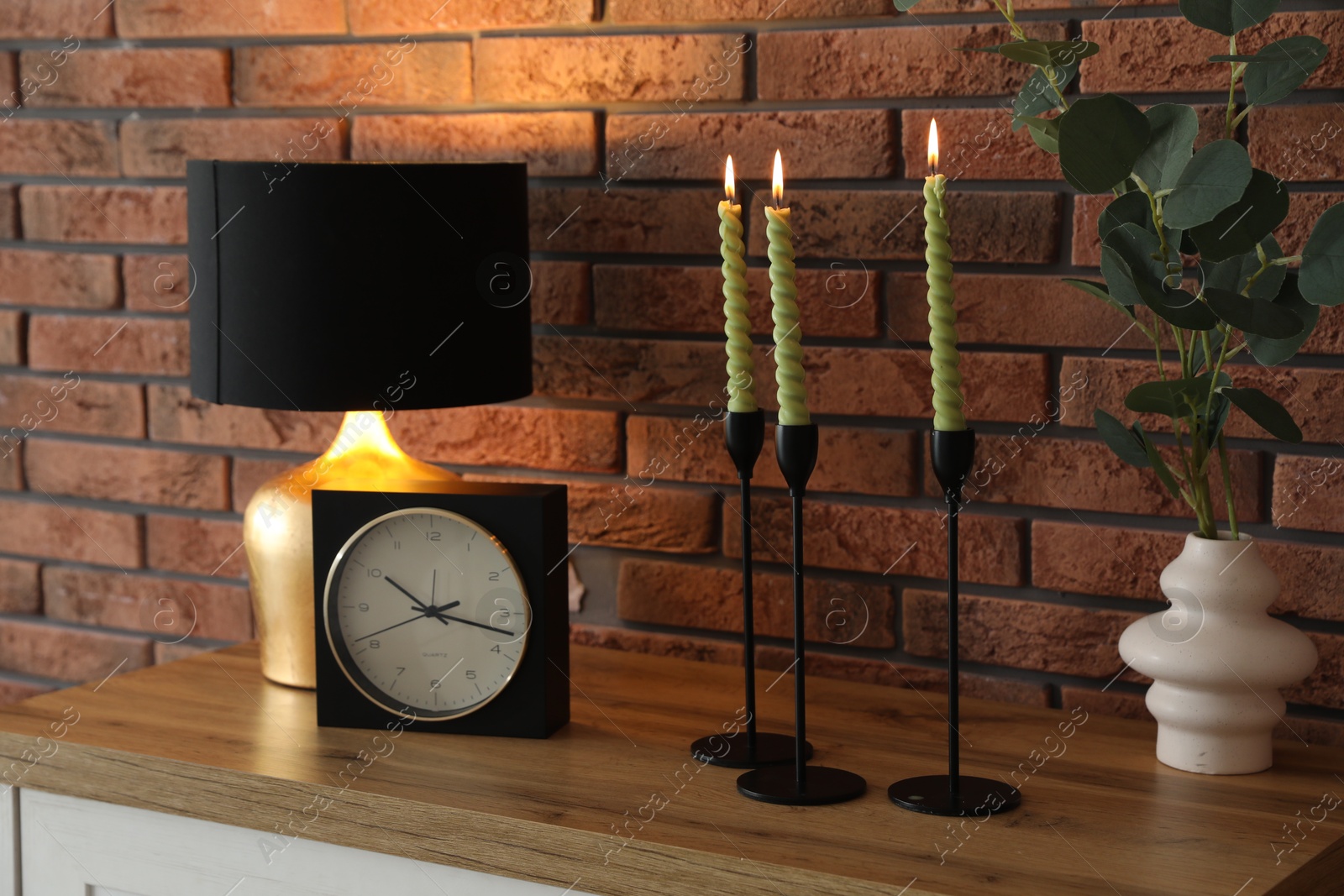 Candlesticks with burning candles on table near brick wall Photo of Candlesticks with burning candles on table near brick wall