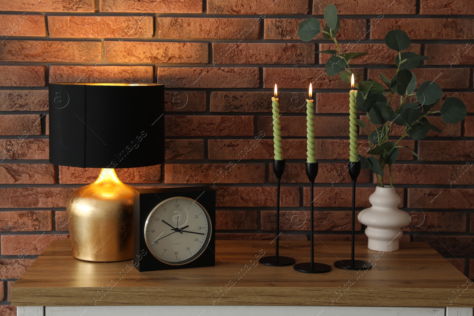 Candlesticks with burning candles on table near brick wall Photo of Candlesticks with burning candles on table near brick wall