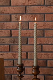 Photo of Candlesticks with burning candles near brick wall, closeup