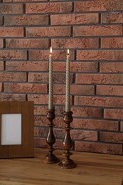 Photo of Candlesticks with burning candles on table near brick wall