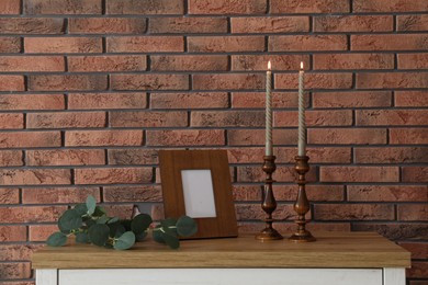 Photo of Candlesticks with burning candles on table near brick wall