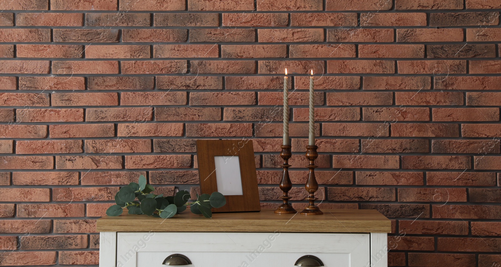 Candlesticks with burning candles on table near brick wall Photo of Candlesticks with burning candles on table near brick wall
