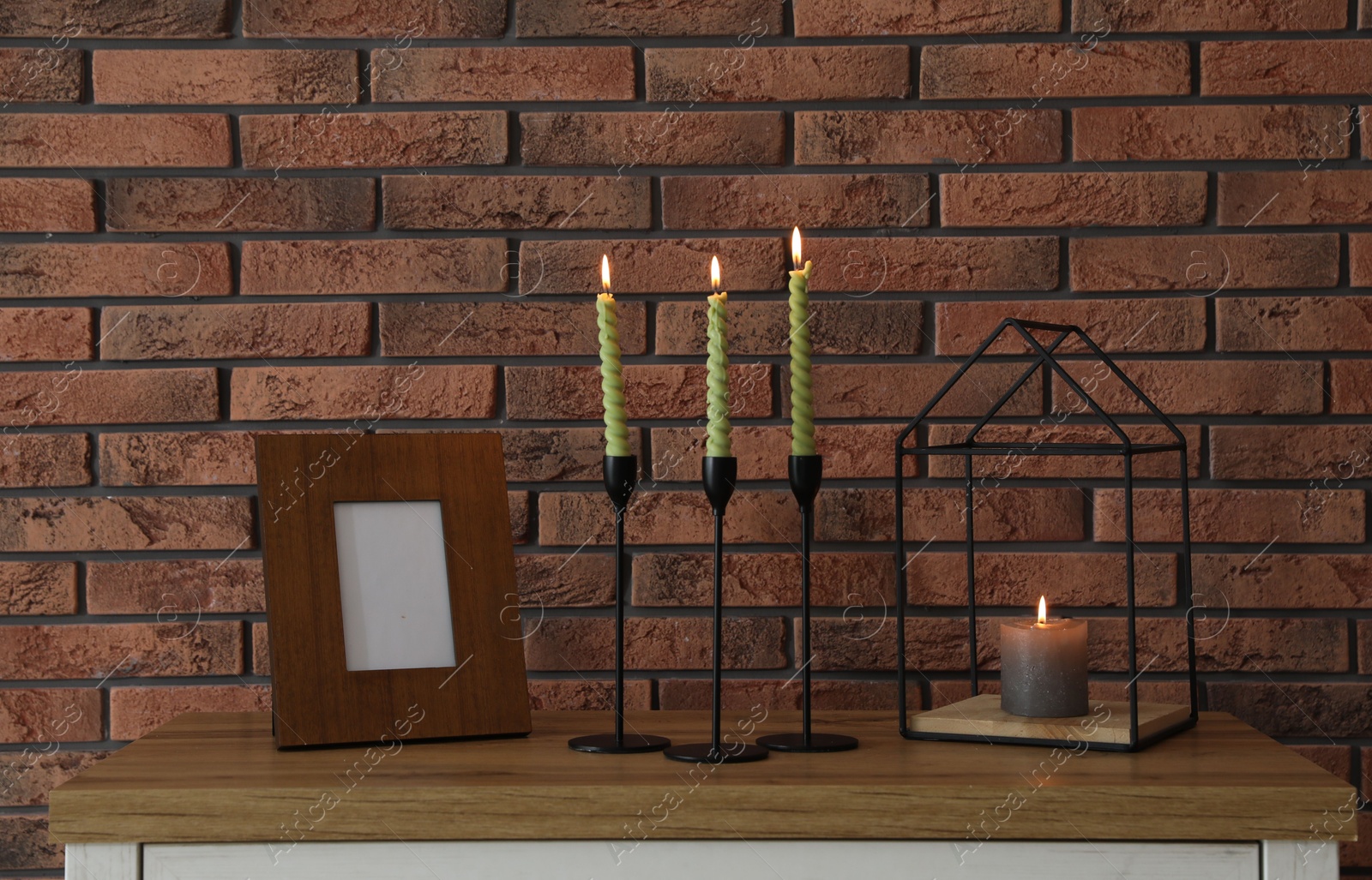Candlesticks with burning candles on table near brick wall Photo of Candlesticks with burning candles on table near brick wall
