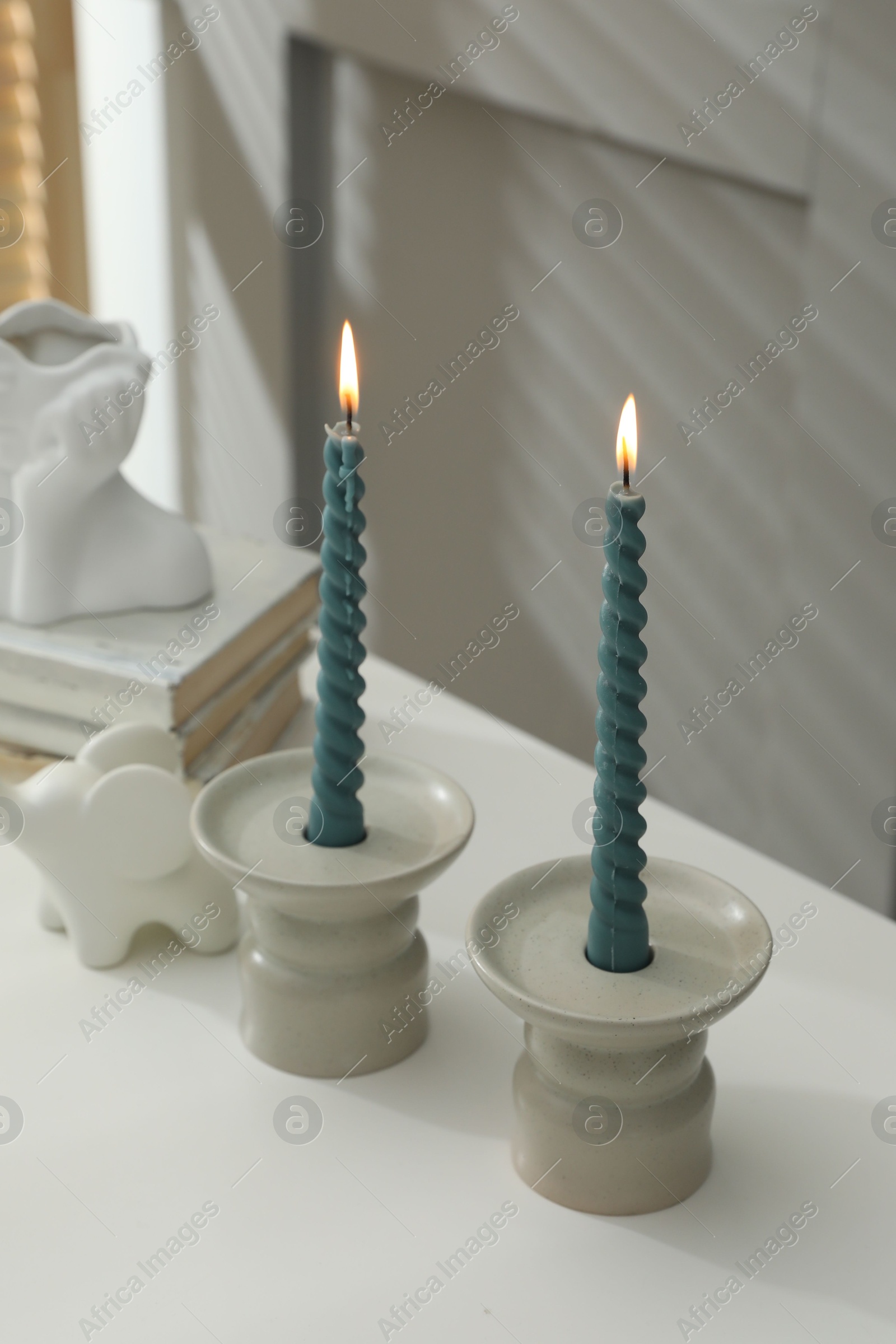 Candlesticks with burning candles on table near grey wall Photo of Candlesticks with burning candles on table near grey wall