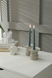 Photo of Candlesticks with burning candles on table near grey wall