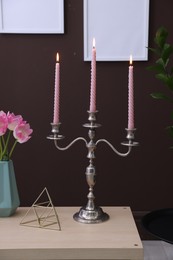 Photo of Elegant candlestick with burning candles and decor on table near brown wall
