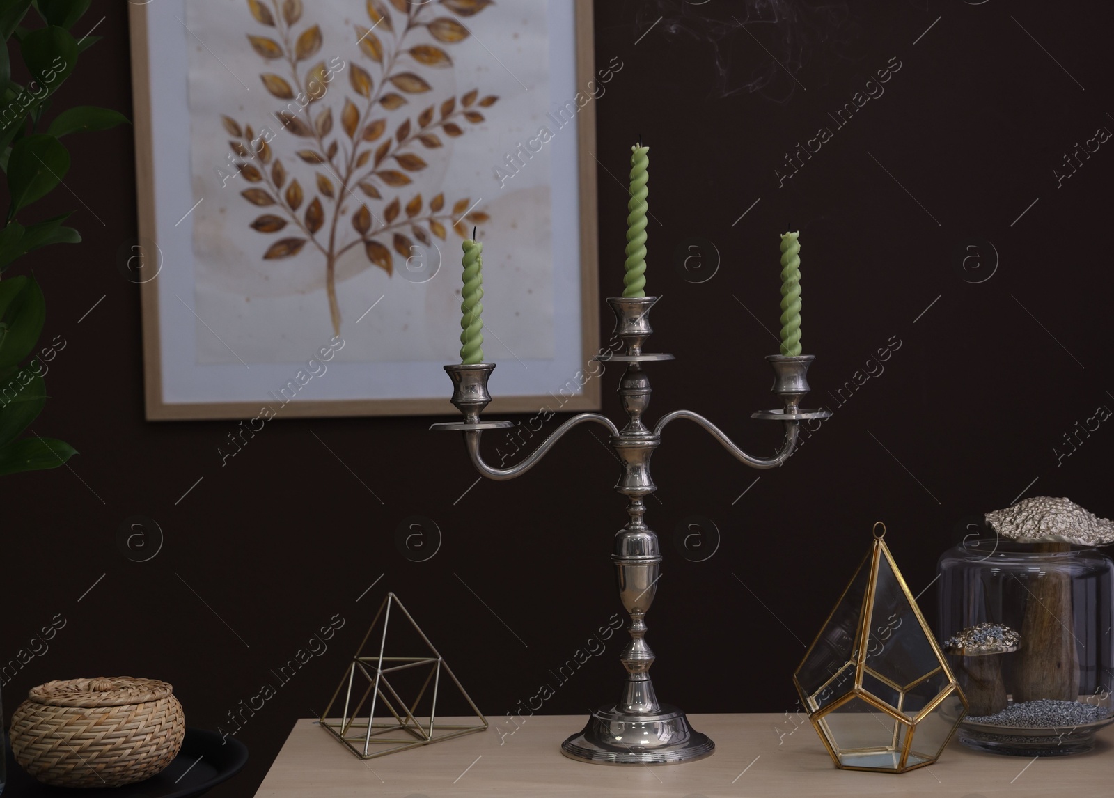 Elegant candlestick with candles and decor on table near brown wall Photo of Elegant candlestick with candles and decor on table near brown wall