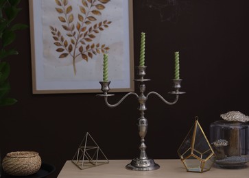 Photo of Elegant candlestick with candles and decor on table near brown wall