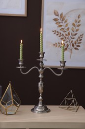 Photo of Elegant candlestick with burning candles and decor on table near brown wall