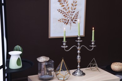 Photo of Elegant candlestick with burning candles and decor on table near brown wall