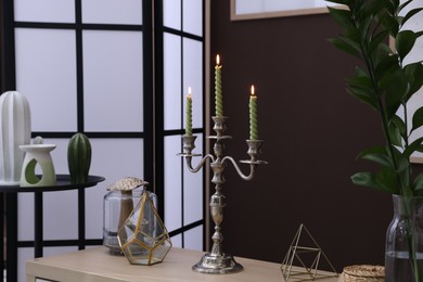 Photo of Elegant candlestick with burning candles and decor on table near brown wall
