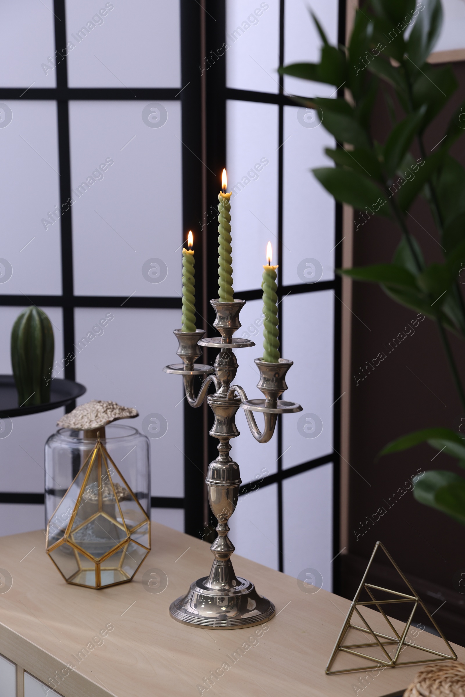 Elegant candlestick with burning candles and decor on table near brown wall Photo of Elegant candlestick with burning candles and decor on table near brown wall