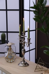 Photo of Elegant candlestick with burning candles and decor on table near brown wall