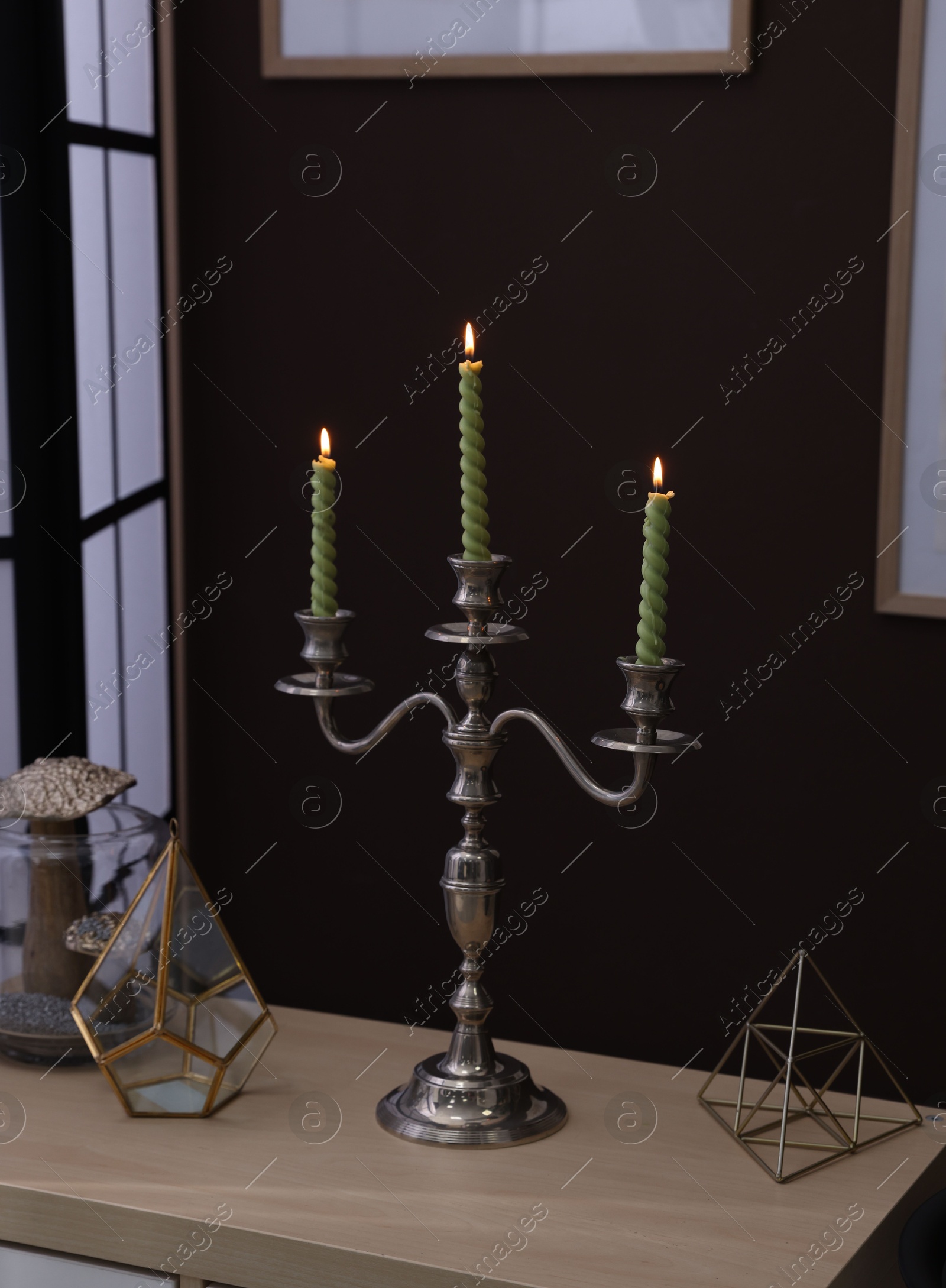Elegant candlestick with burning candles and decor on table near brown wall Photo of Elegant candlestick with burning candles and decor on table near brown wall