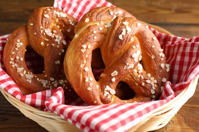 Photo of Tasty pretzels with salt in wicker basket on wooden table, closeup