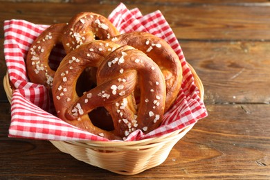 Photo of Tasty pretzels with salt in wicker basket on wooden table, closeup. Space for text