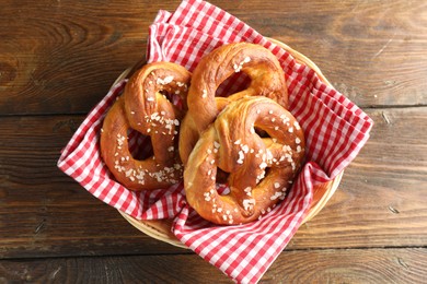 Photo of Tasty pretzels with salt in wicker basket on wooden table, top view