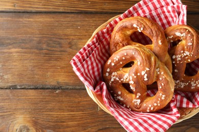 Photo of Tasty pretzels with salt in wicker basket on wooden table, top view. Space for text