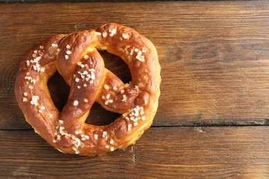 Photo of Tasty pretzel with salt on wooden table, top view. Space for text