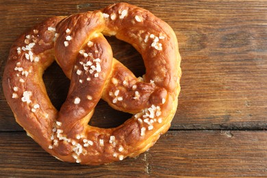 Photo of Tasty pretzel with salt on wooden table, top view. Space for text
