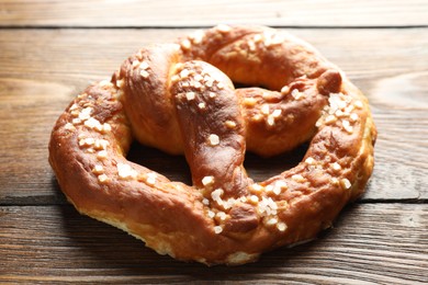 Photo of Tasty pretzel with salt on wooden table, closeup