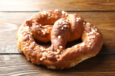 Photo of Tasty pretzel with salt on wooden table, closeup