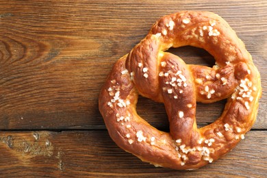 Photo of Tasty pretzel with salt on wooden table, top view. Space for text