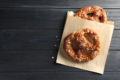 Photo of Tasty pretzels with salt on dark wooden table, top view. Space for text