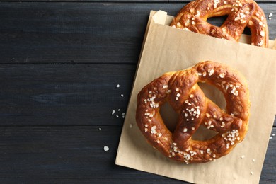 Photo of Tasty pretzels with salt on dark wooden table, top view. Space for text