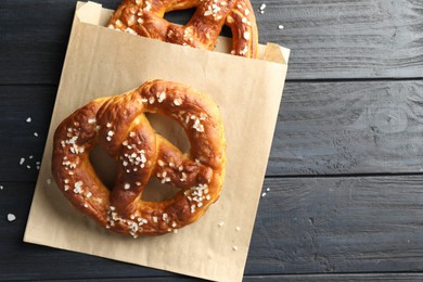Photo of Tasty pretzels with salt on dark wooden table, top view. Space for text