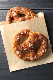 Photo of Tasty pretzels with salt on dark wooden table, top view