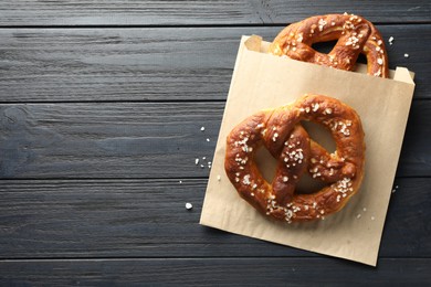 Photo of Tasty pretzels with salt on dark wooden table, top view. Space for text
