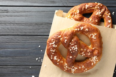 Photo of Tasty pretzels with salt on dark wooden table, top view. Space for text