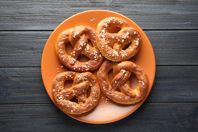 Photo of Tasty pretzels with salt on dark wooden table, top view