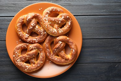 Photo of Tasty pretzels with salt on dark wooden table, top view. Space for text