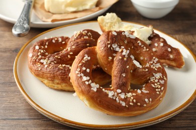 Photo of Tasty pretzels with salt and butter on wooden table, closeup