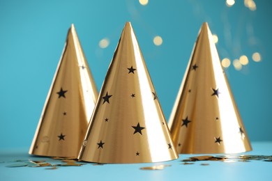 Photo of Beautiful party hats and confetti on light blue background. Bokeh effect