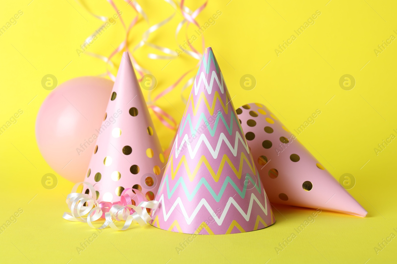 Beautiful party hats, balloon and streamers on yellow background Photo of Beautiful party hats, balloon and streamers on yellow background