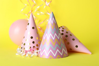 Photo of Beautiful party hats, balloon and streamers on yellow background