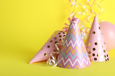 Photo of Beautiful party hats, balloon and streamers on yellow background, space for text