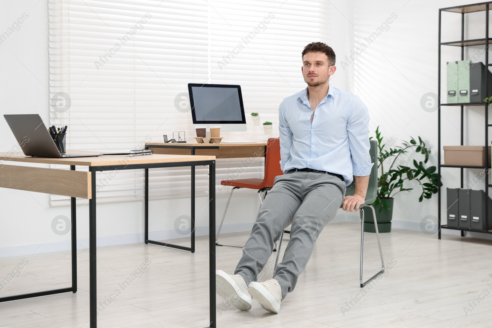 Handsome man exercising with chair in office Photo of Handsome man exercising with chair in office