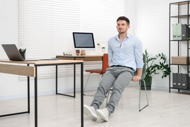 Photo of Handsome man exercising with chair in office