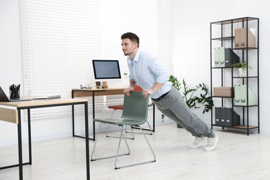 Photo of Handsome man exercising with chair in office