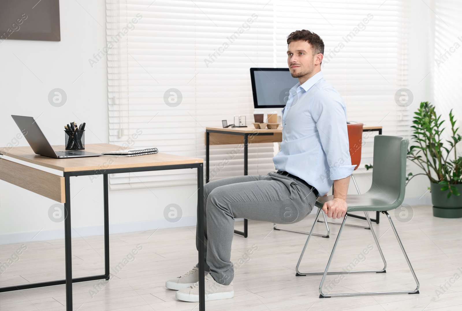 Handsome man exercising with chair in office Photo of Handsome man exercising with chair in office