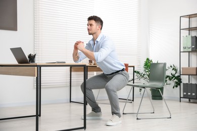 Photo of Handsome man doing exercise near desk in office