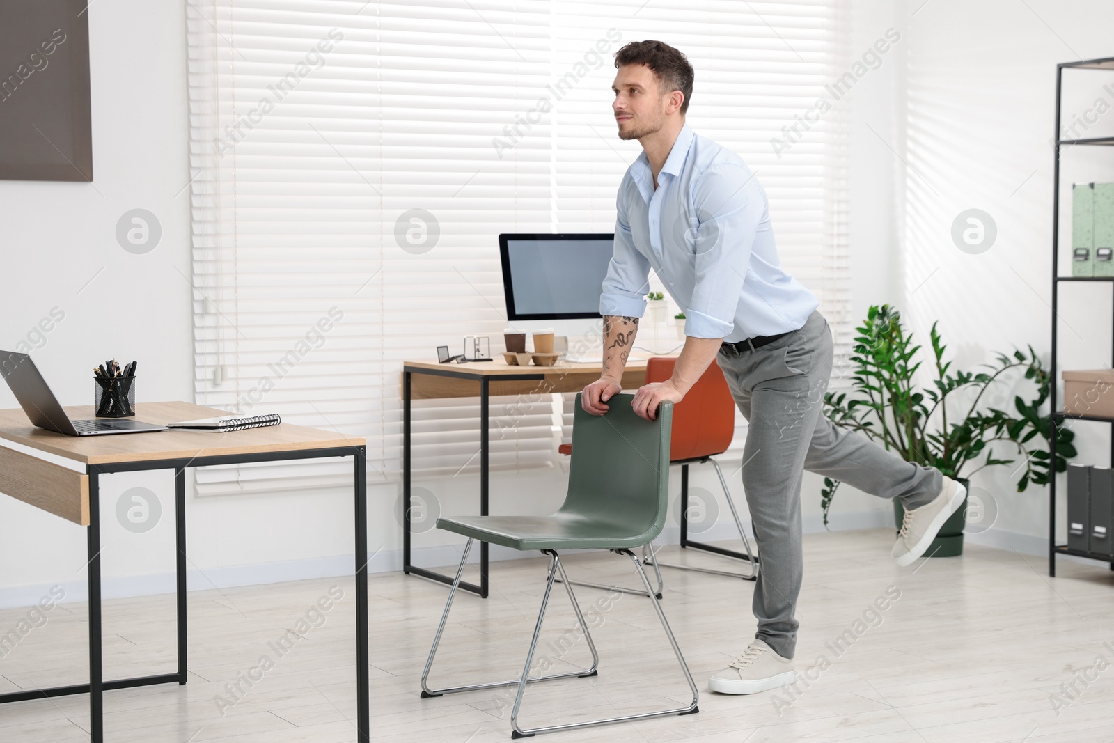 Handsome man exercising with chair in office Photo of Handsome man exercising with chair in office