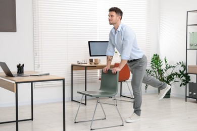 Photo of Handsome man exercising with chair in office
