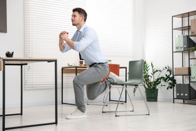 Photo of Handsome man exercising with chair in office