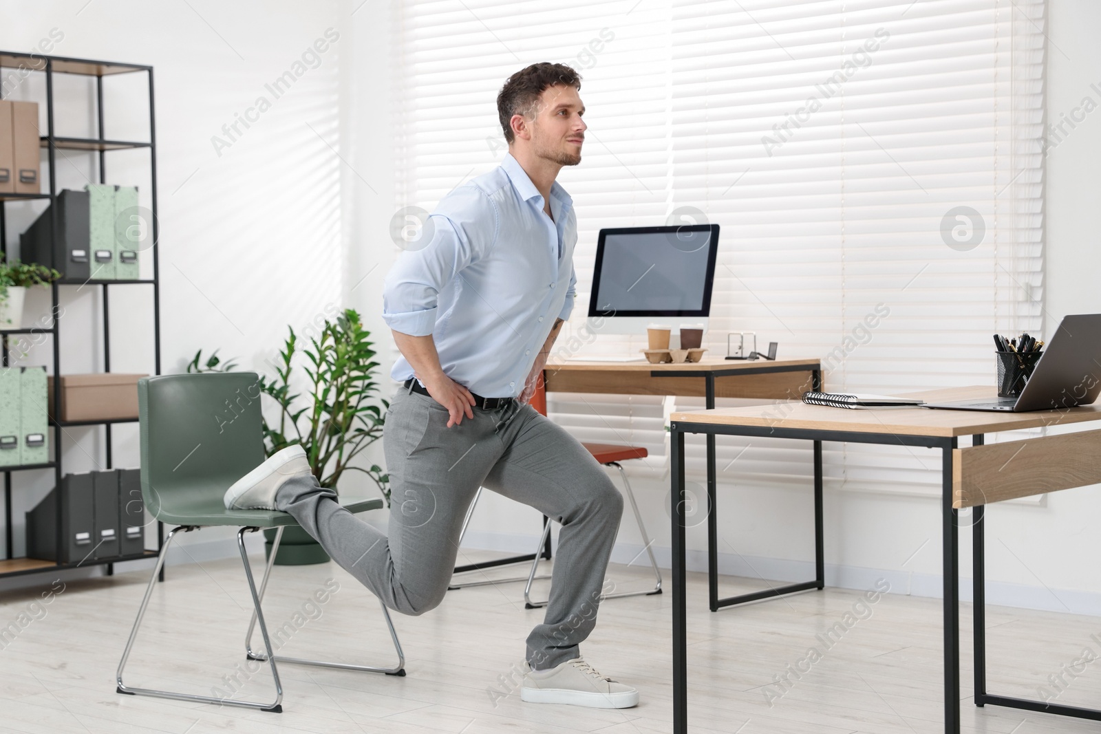 Handsome man exercising with chair in office Photo of Handsome man exercising with chair in office